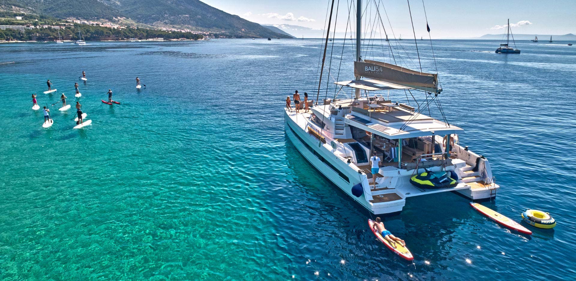Bali 5.4 catamaran at anchor off Brač with paddle-boarders around it