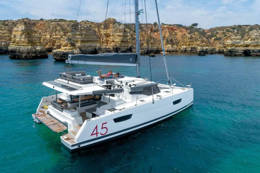 A 45 ft catamaran with a flybridge lounge at anchor below cliffs