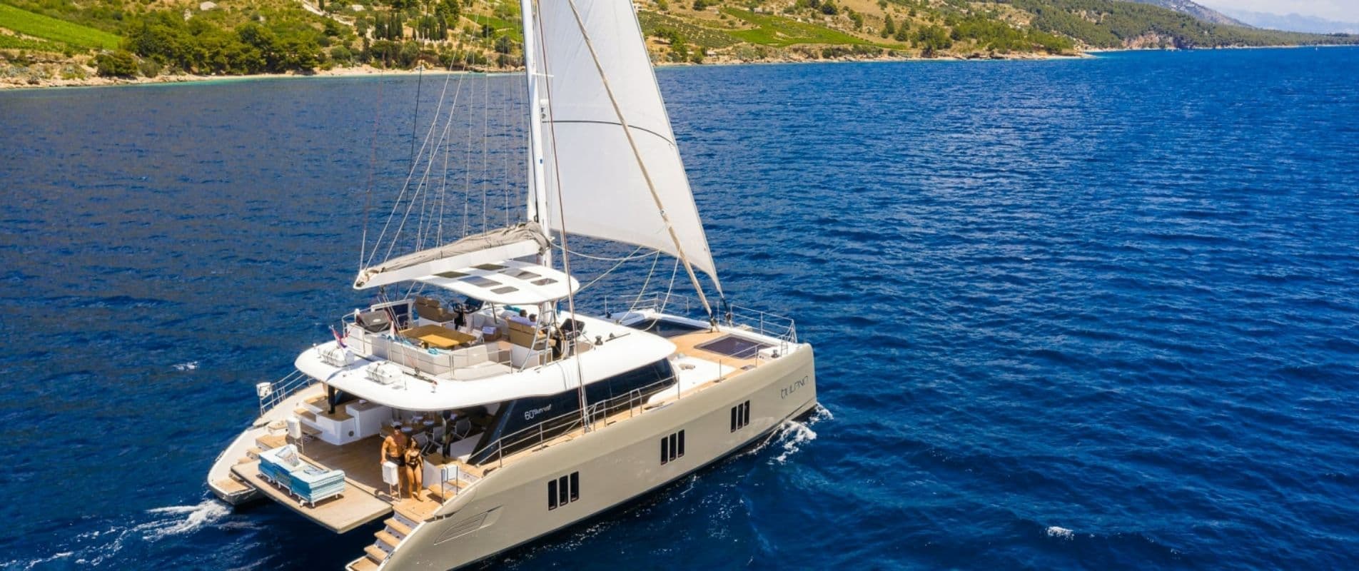 A 60 ft luxury sailing catamaran under sail off a wooded coast