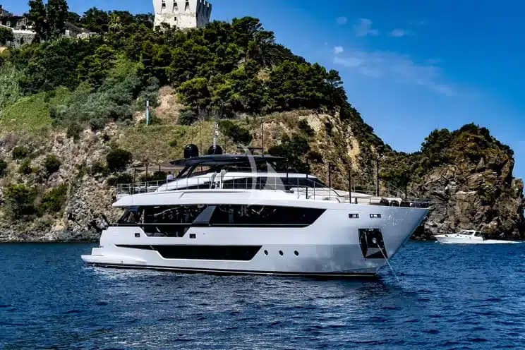 A large motor yacht at anchor below a wooded headland