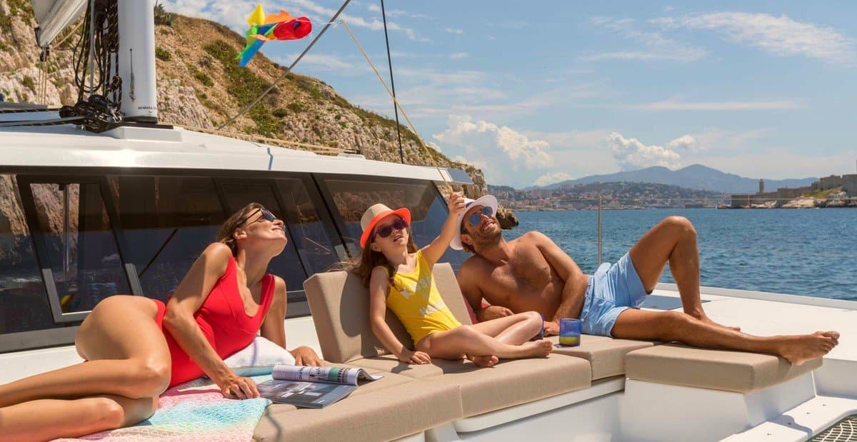 Three guests sunbathing on the foredeck of a catamaran at anchor