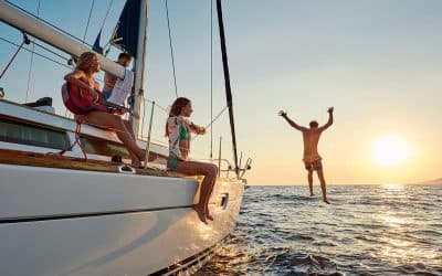 Friends on the deck of a sailboat at sunset, one jumping into the sea
